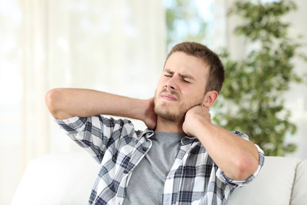 What Trauma Therapy in Ottawa Actually Looks Like—And How to Know If You Need It. Man suffering neck pain sitting on a sofa in the living room at home.